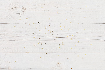 Top view on a lot of small golden stars confetti on old white wooden background. Holiday and celebration concept