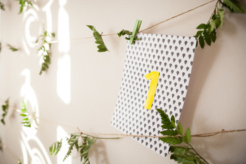 Light background of a wall decorated with leaves of fern on a string and a card with the number 1