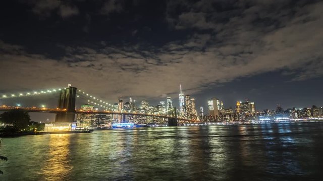 The famous Brooklyn Bridge in the evening, ships sail along the river, in the background the luminous skyscrapers of Manhattan