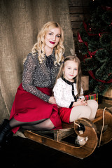 Beautiful happy mother and daughter with Christmas winter sleigh in the decorative interior of the New Year with a festive Christmas tree and Christmas decorations having fun
