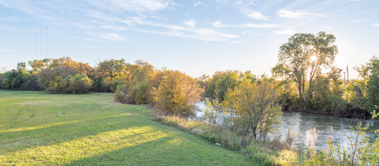 Panorama view beautiful riverside park with fall foliage vibrant color and sun peeking through trees in Carrollton, Texas, USA. Stunning yellow autumn leaves at sunset © trongnguyen