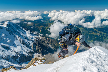 Extreme alpinist in high altitude on Aiguille de Bionnassay mountain summit, Mont Blanc massif,...