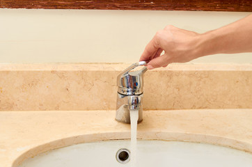 marble sink with chromed faucet and hand, bathroom background