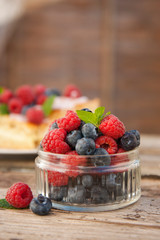 Small glass bowl full of blueberries and raspberries, ready to eat, placed on rustic wood desk.