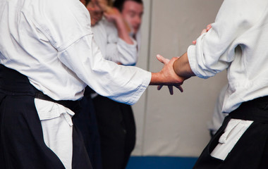 Aikido athletes in white kimono train on blue tatami