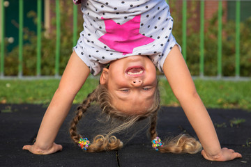Little girl stands on her hands and smiles.