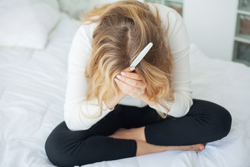 Positive pregnancy test. Young woman feeling depressed and sad after looking at pregnancy test result at home