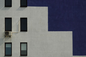 Wall of high-rise bulding in purple and white colours with conditioner and windows.