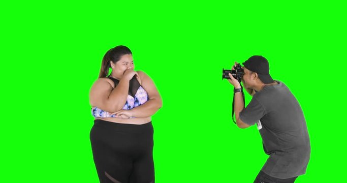 Overweight female model smiling and posing in a photoshoot session with a photographer in the studio. Shot in 4k resolution with green screen background