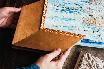 Choosing decorative frame for a painting. Woman's hands and sample of gold wooden frame.