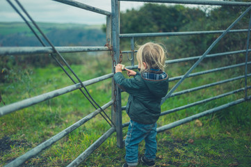 Little toddler standing by fence in the countryside