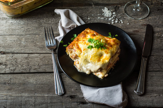 Piece of tasty hot lasagna with red wine. Small depth of field. Traditional italian lasagna. Portion. Italian food. Food on black plate. Bolognese sauce. Bechamel sauce. Still life of food.