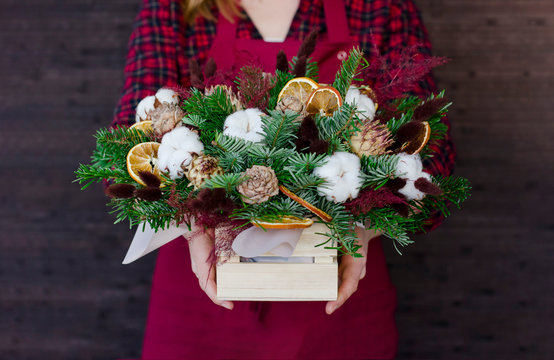 The composition of fir branches and cones in wooden box in the woman hands
