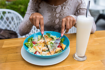 Close up attractive woman hand holding fork and spoon to eating vegetable salad with a cup of milkshake at lunch in cafe. Healthy and vegetarian food.