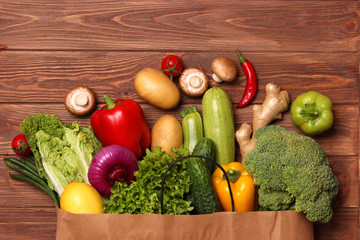 Fresh vegetables in a paper bag on a wooden table. Top view.
