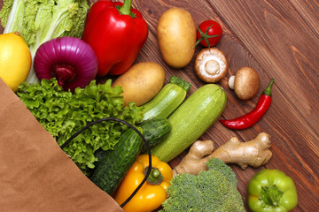 Fresh vegetables in a paper bag on a wooden table. Top view.