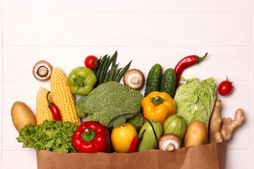 Fresh vegetables in a paper bag on a wooden table. Top view.