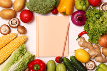 Different fresh vegetables and paper notepad on a wooden table. Top view. Write a recipe, shopping...