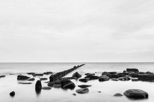 Fototapeta Blabk and white long exposure landscape with poles and stones in the water.