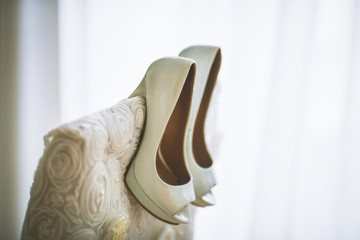 White wedding shoes hanging on the back of a white chair