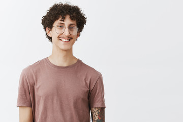 Studio shot of charming motivated good-looking curly-haired guy with moustache and tattooed arm in...