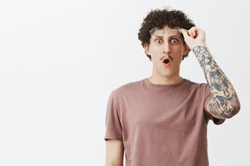 Man never seen such incredible tattoo. Surprised and impressed speechless amazed guy with moustache and curly hairstyle dropping jaw saying wow taking off glasses staring astonished at camera