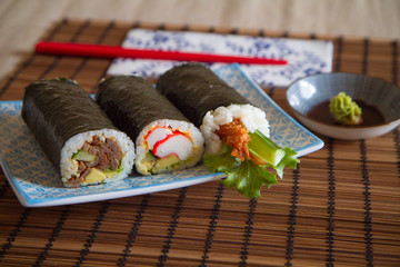 three sushi rolls on a plate with soy sauce and chopsticks