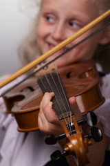 Cute little girl in bright blouse plays the violin close-up on a gray background