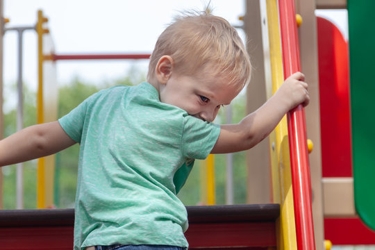 Funny cute caucasian blonde baby boy plays on the playground, climbing to upstair. The emotion of happiness, fun, joy. Outdoor, copy space.