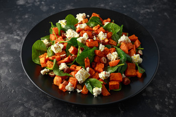 Healthy roasted sweet potato salad with spinach, feta cheese, hazelnut nuts in black plate