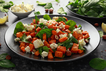 Healthy roasted sweet potato salad with spinach, feta cheese, hazelnut nuts in black plate
