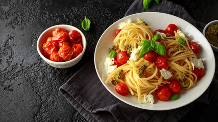 Pasta with green pesto sauce, roasted cherry tomatoes and mozzarella cheese in white plate on dark rustic background