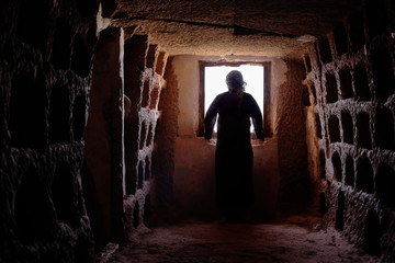 Fototapeta na wymiar MAN WITH TUNIC AND PALESTINIAN SCARF IN A OLD CAVE LOOKING FOR A WINDOW
