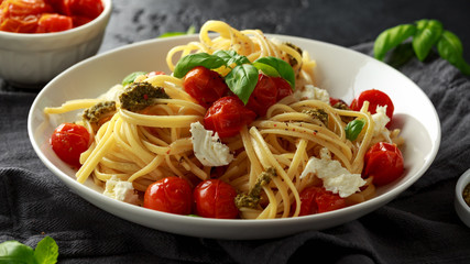 Pasta with green pesto sauce, roasted cherry tomatoes and mozzarella cheese in white plate on dark rustic background