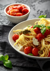 Pasta with green pesto sauce, roasted cherry tomatoes and mozzarella cheese in white plate on dark rustic background