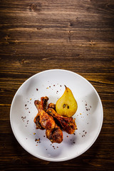 Grilled chicken drumsticks with pear on wooden background