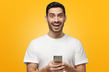 Young laughing man holding smartphone in hands, isolated on yellow background