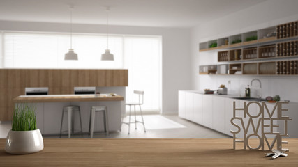 Wooden table, desk or shelf with potted grass plant, house keys and 3D letters making the words home sweet home, over contemporary kitchen, interior design, blur background