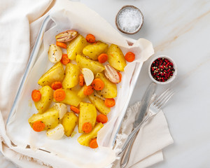 Colorful roasted vegetables on tray with parchment. Potatoes, carrots and onions. Bright marble table. Top view