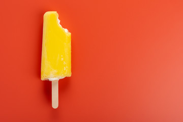yellow popsicle with a bite on an orange color background