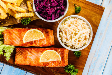 Grilled salmon with french fries and vegetables served on cutting board on wooden table