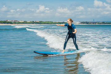 Joyful young woman beginner surfer with blue surf has fun on small sea waves. Active family...