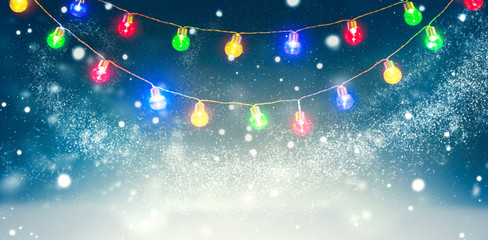 Winter holiday snow background decorated with colorful light bulbs garland. Snowflakes. Christmas...