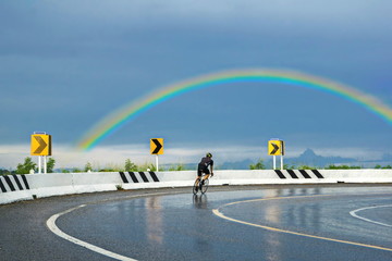 Beautiful rainbow in thailand. People are biking along the scenic road.Competitive cycling on the road. Bicycle Race. Cycling exercise.