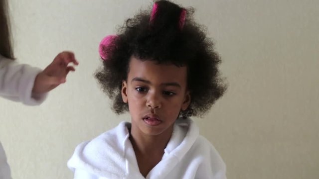 Black girl wind curlers in her hair. Little girls play with hair curlers and hairpins.