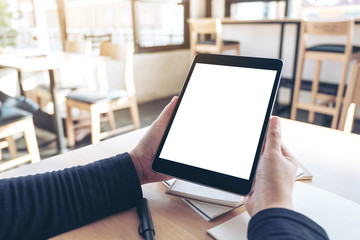 Mockup image of hands holding and using black tablet pc with blank white desktop screen while working on notebooks in office
