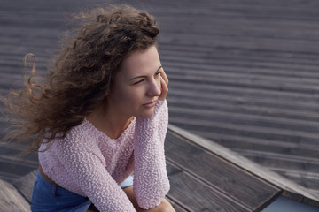 Authentic portrait of young Caucasian attractive female, watching  sunset, looking afar. Wind is...