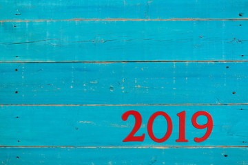 Year 2019 in bold red on blank antique rustic teal blue wood background; message board with New Year holiday concept and painted copy space