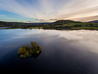 Aerial panoramic view of a beautiful natural lake in Brecon Beacons surrounded by rural farmland (Llangorse Lake, Wales)