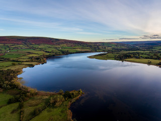 Aerial panoramic view of a beautiful natural lake in Brecon Beacons surrounded by rural farmland (Llangorse Lake, Wales)